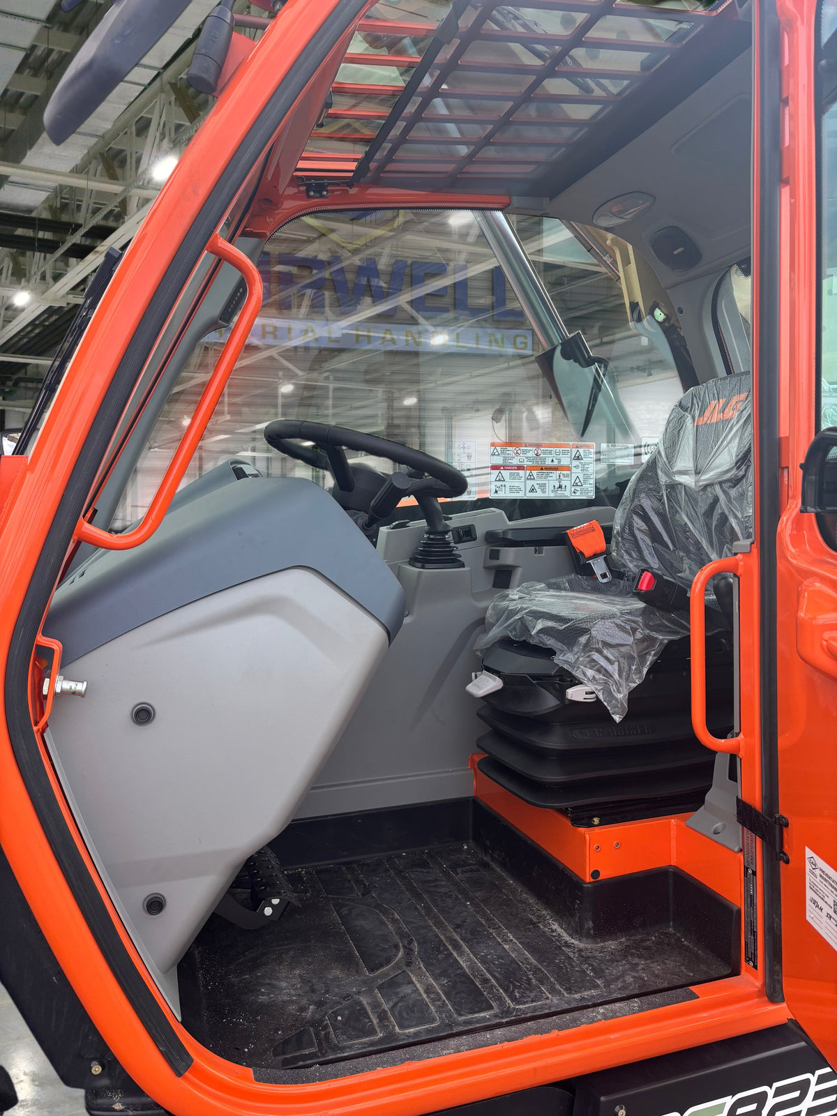 Interior view of a 2024 JLG 823 Ag Telehandler cabin at Burwell Material Handling with an orange frame and grey seat.
